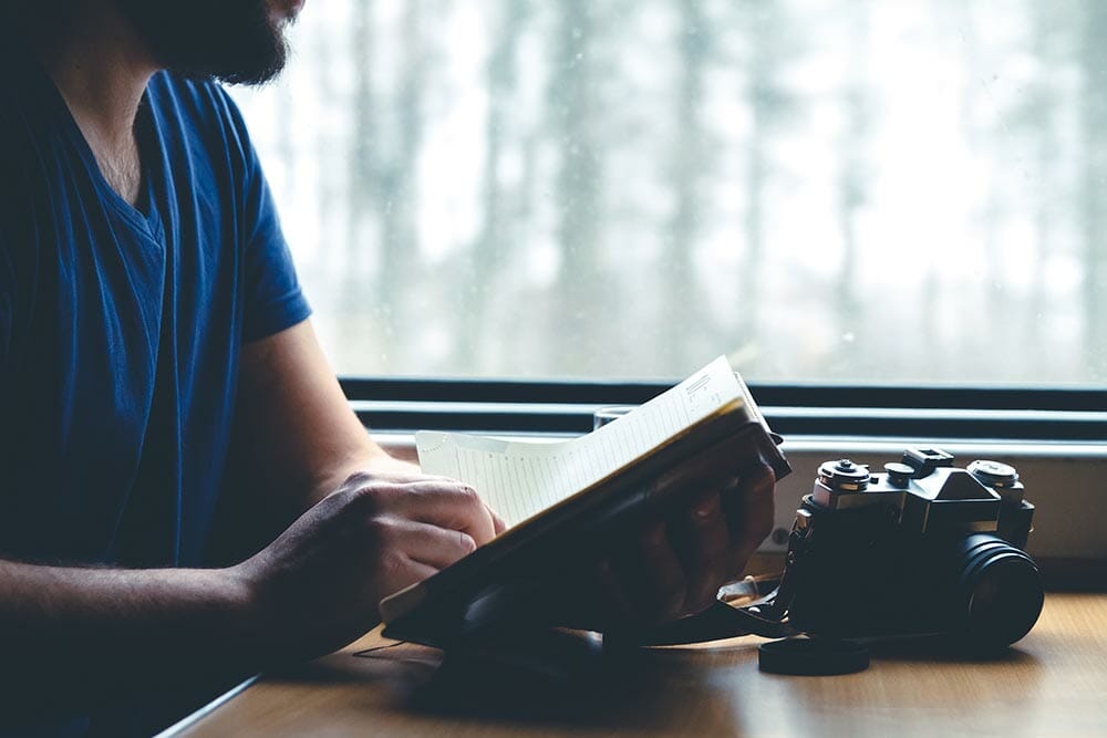 The man sits at a table in a train, looking into the notebook