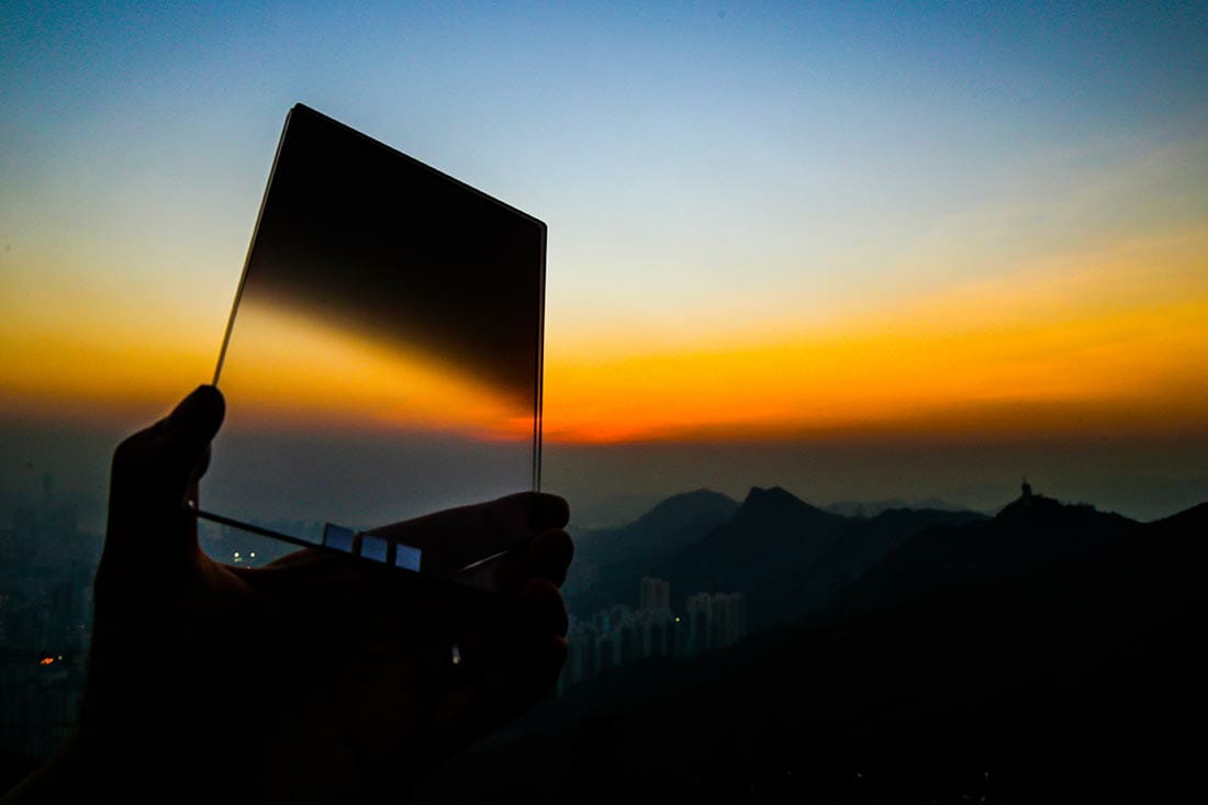 A hand outstretched holding a graduated neutral filter during sunset