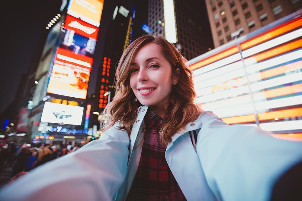 Young happy woman taking selfie on Times Square at night, Manhattan. Inspiring New York atmosphere and a beautiful smiling girl.