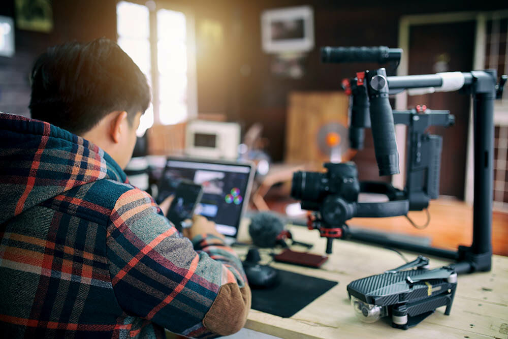 Young freelancer man editing video on laptop and checking smartphone for uploading video to internet online or social media.