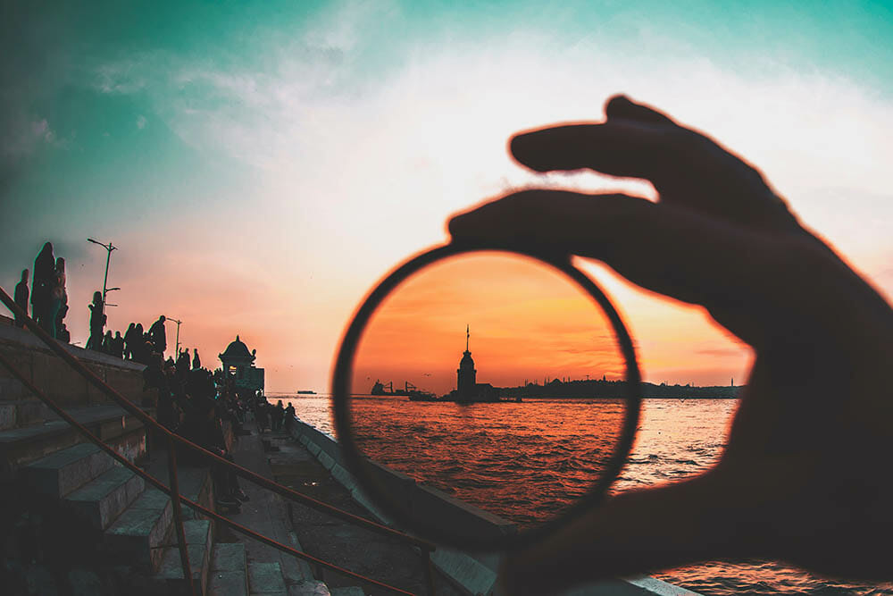 a man holding a photo filter with background of Maiden Tower during sunset