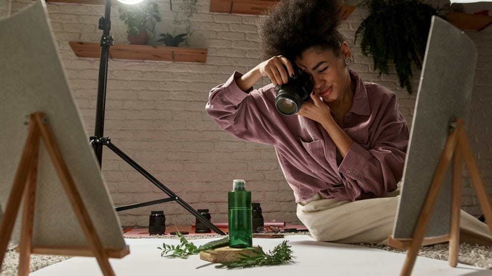 Black female photographer taking photo of aloe vera leaf, branches and lotion on this plants on digital camera at home studio. Beauty and body care content for photostocks, commerce, social networks