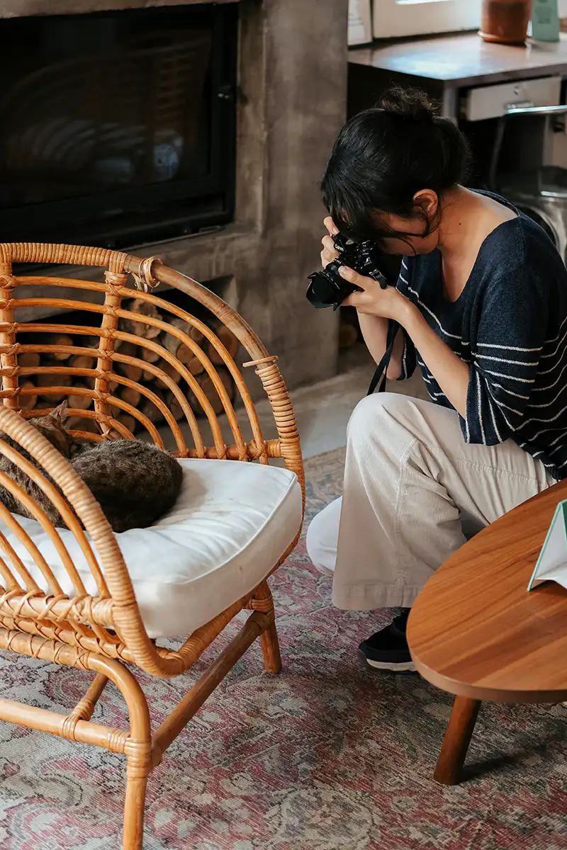 A woman with a digital camera photographing a cat lying on a chair