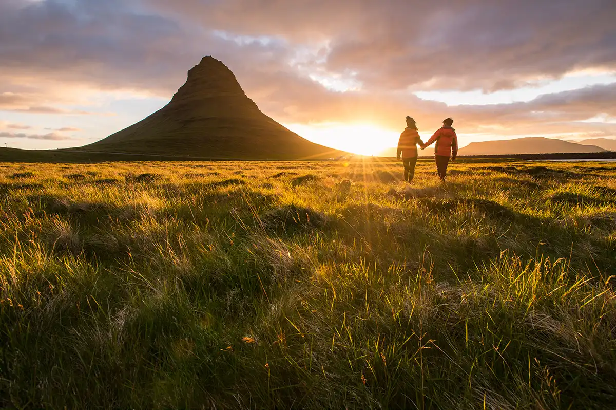 Sunset behind a mountain with two people walking in a field holding hands