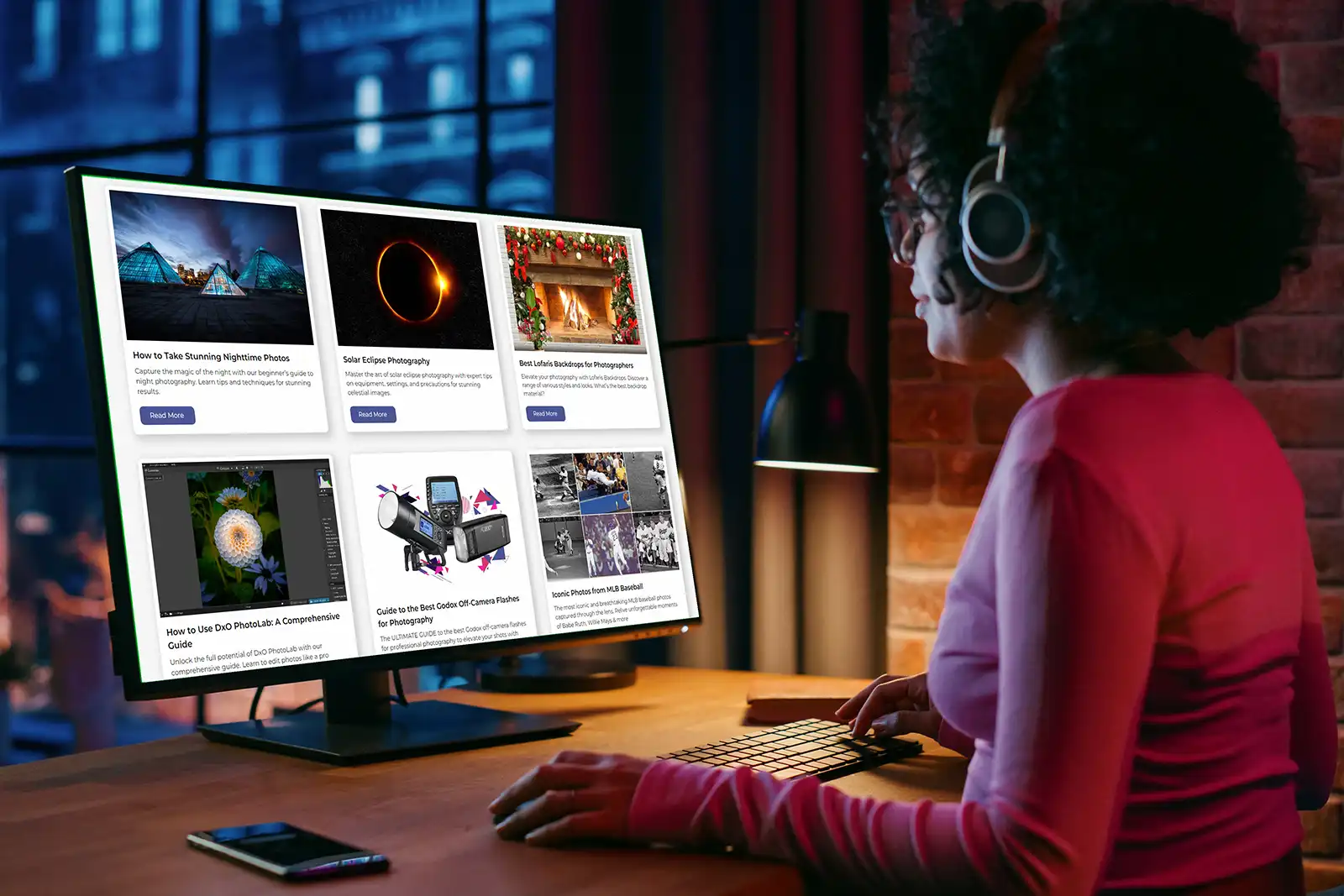 Woman sat a computer at night wearing headphones looking at a website called iPhotography.com