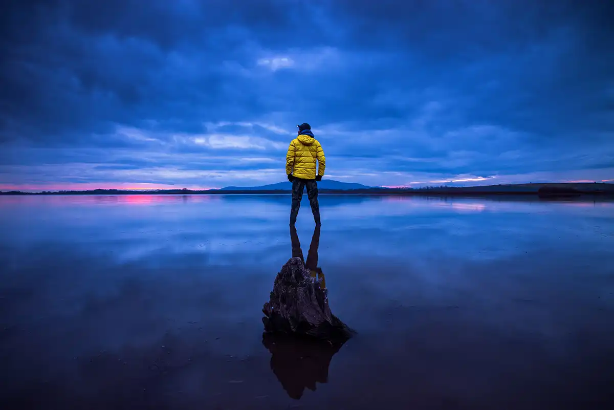 a man in a yellow jacket looking towards the horizon during blue hour