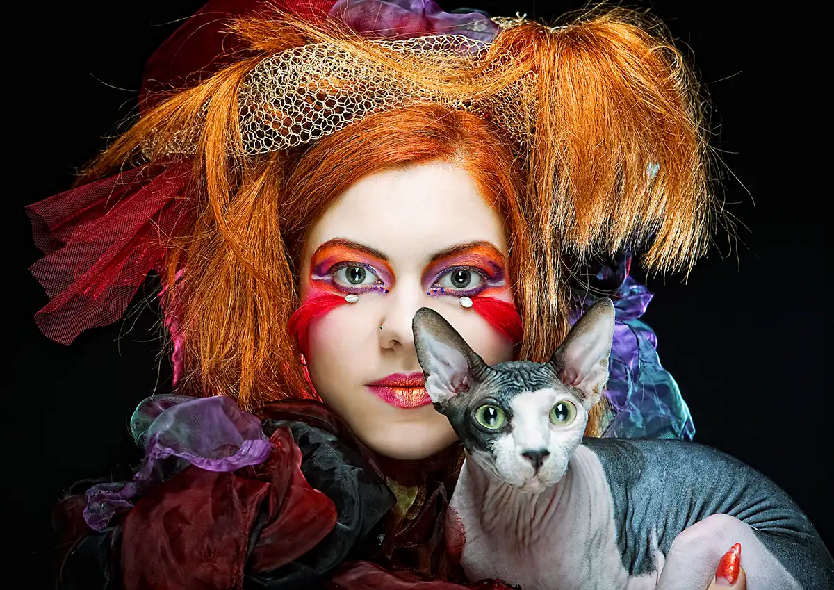 A high fashion portrait of a model looking at a camera with red hair dramatic make up holding a cat