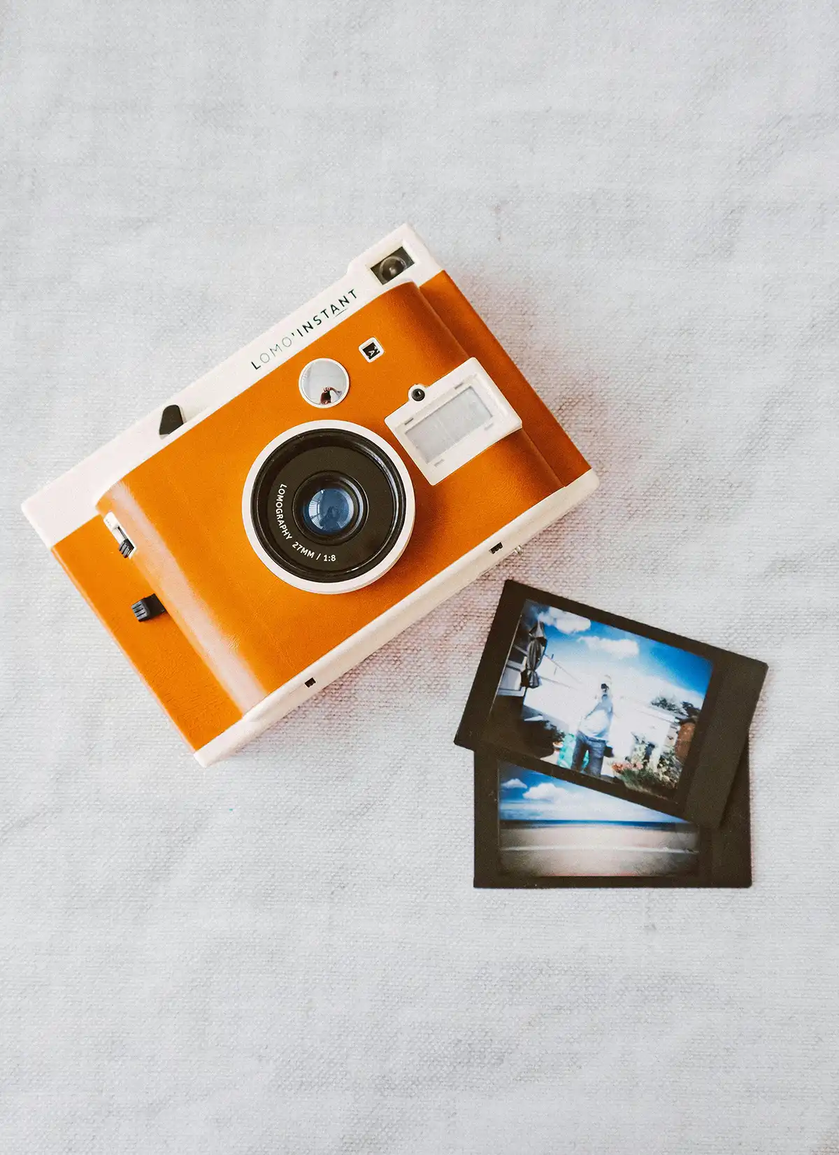 Orange retro camera with print photos from an overhead view
