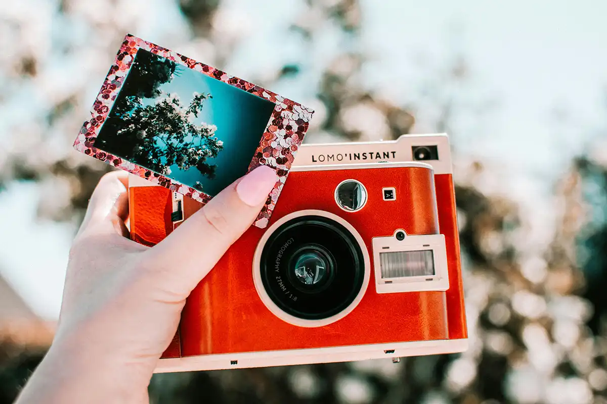 Hand holding a red retro camera and a mini print