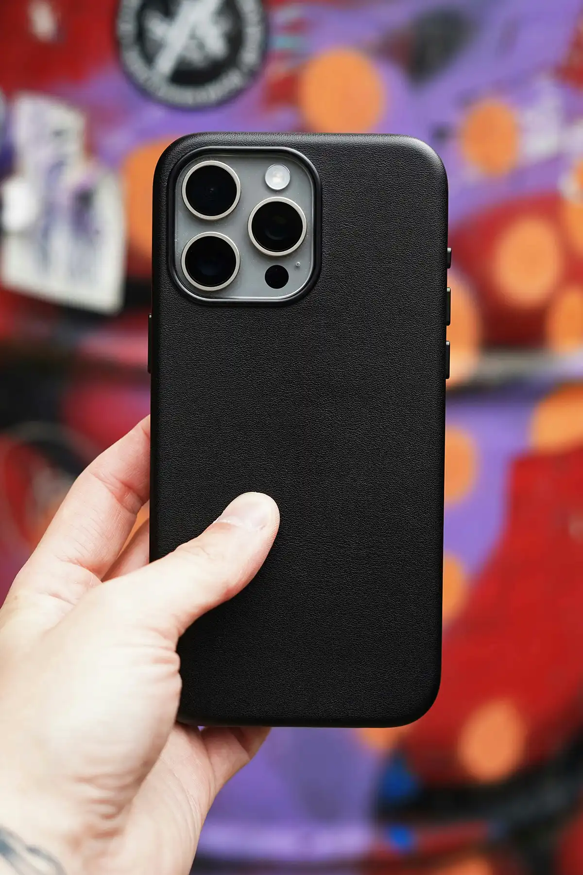 iPhone with a black case being held in a hand against a graffiti wall
