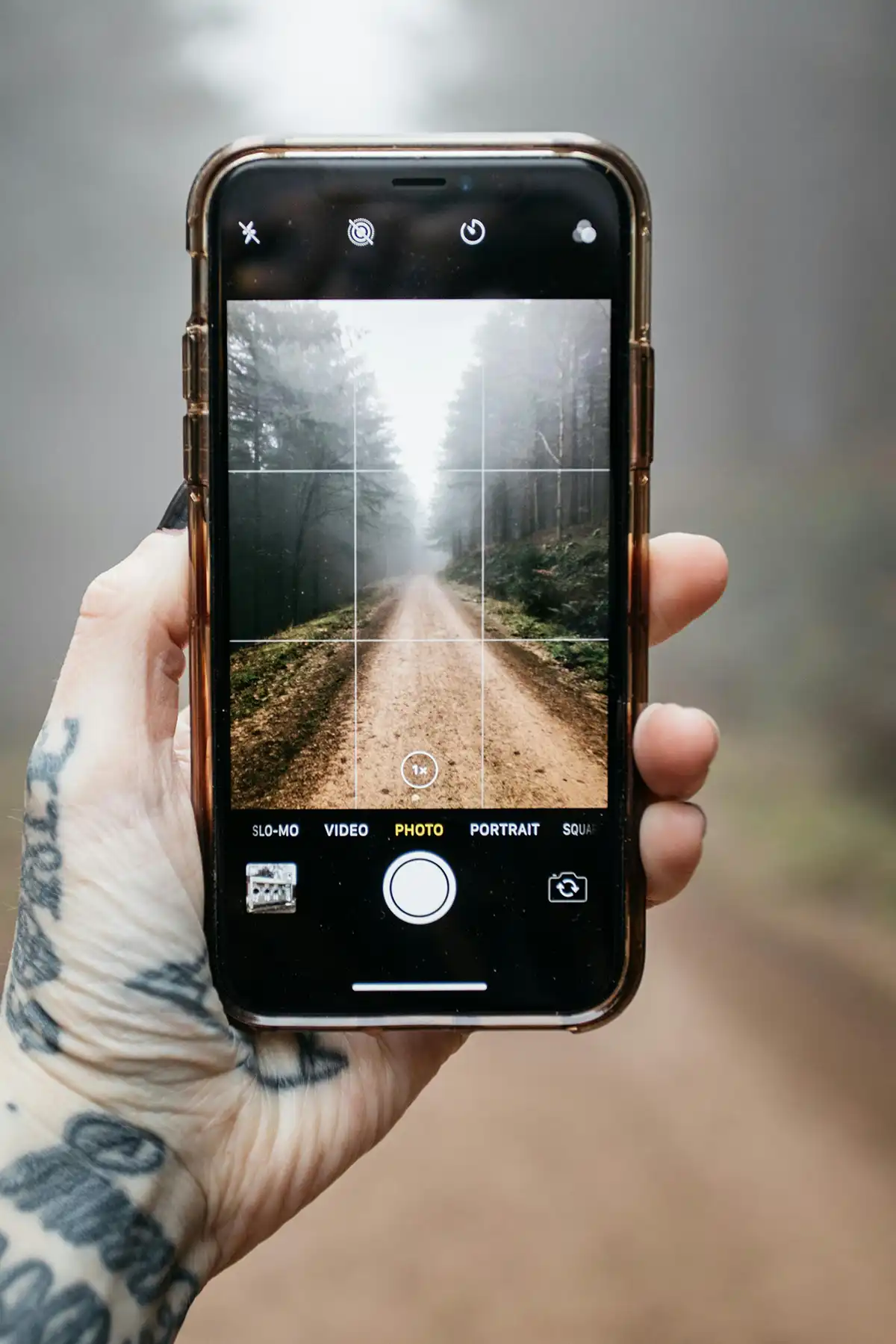 Person holding a smartphone vertically, capturing a photo of a path leading into the distance.