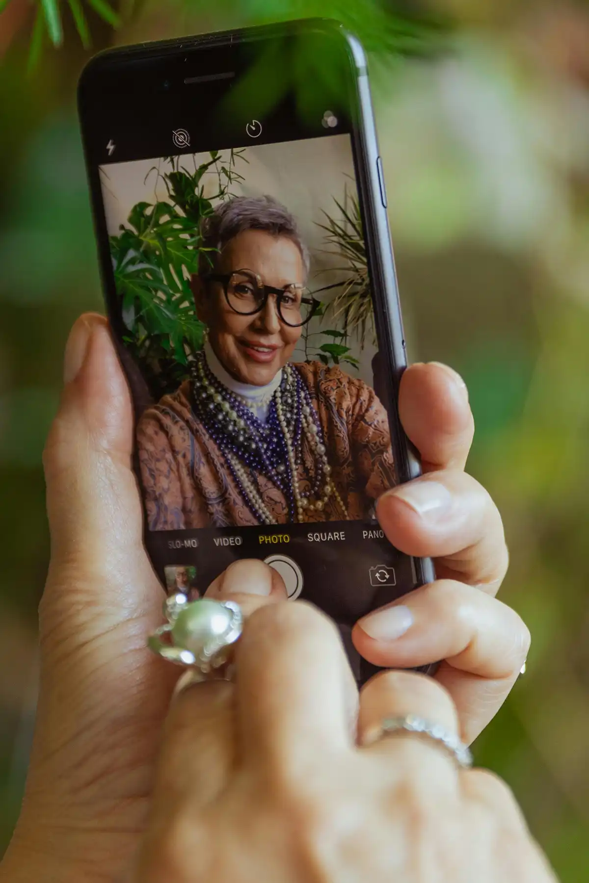 Hands holding iPhone with a photo of a lady wearing glasses on screen