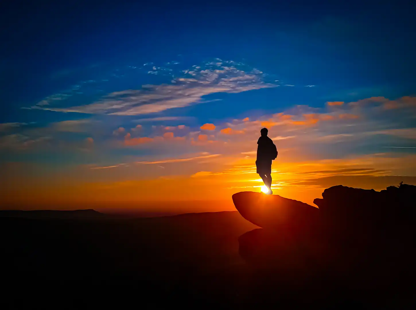 person stood on a rocky outcrop overlooking a sunset