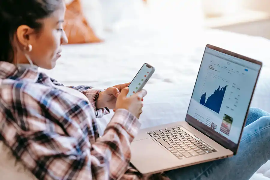 lady holding a phone looking at a laptop