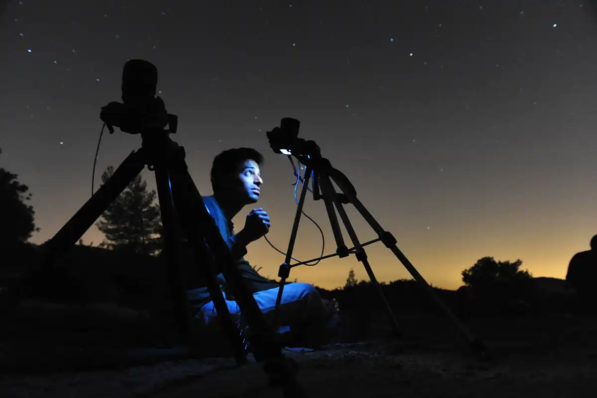 a man sat on the floor looking at the back of a camera in the dark photographing the moon