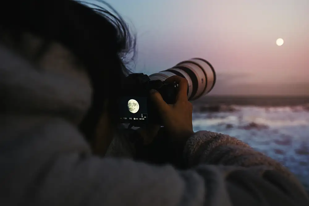 Over the shoulder photo of a photographer taking a photo of the moon over the sea