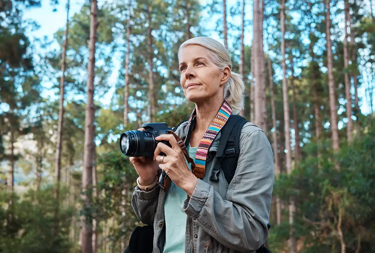 older woman holding a digital camera in woodland