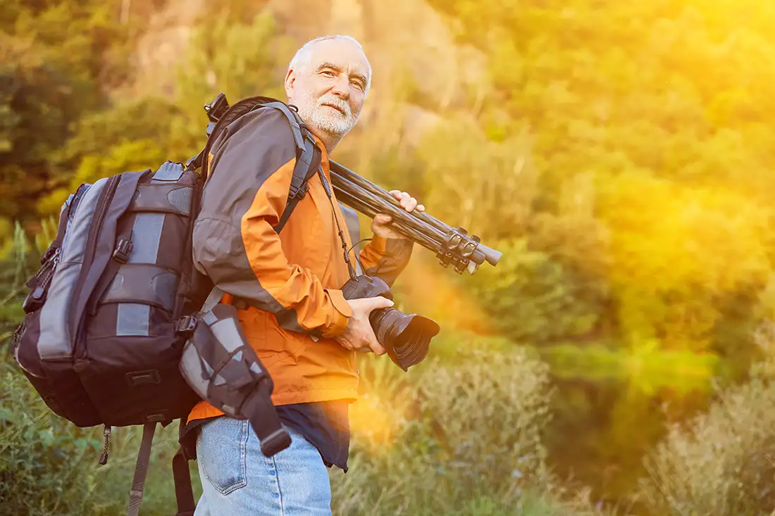 A Photographer with camera and tripod in hand wearing a backpack and in an orange coat