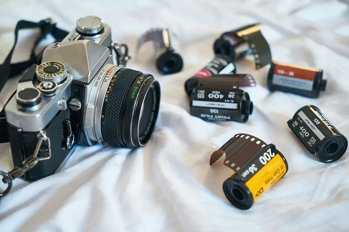 A vintage film camera on a white blanket with 35mm film cannisters surrounding