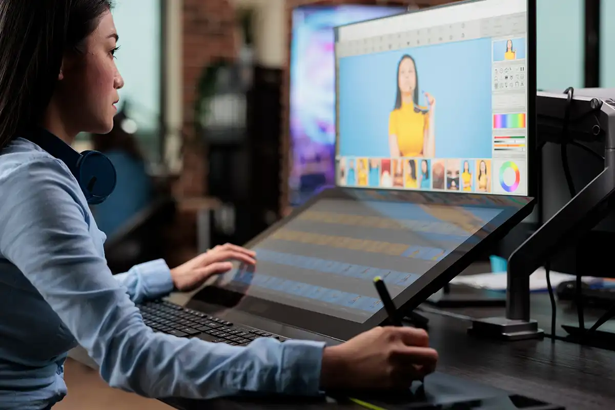 A digital retoucher sat at a desk retouching photos on a computer using a graphic stylus pen
