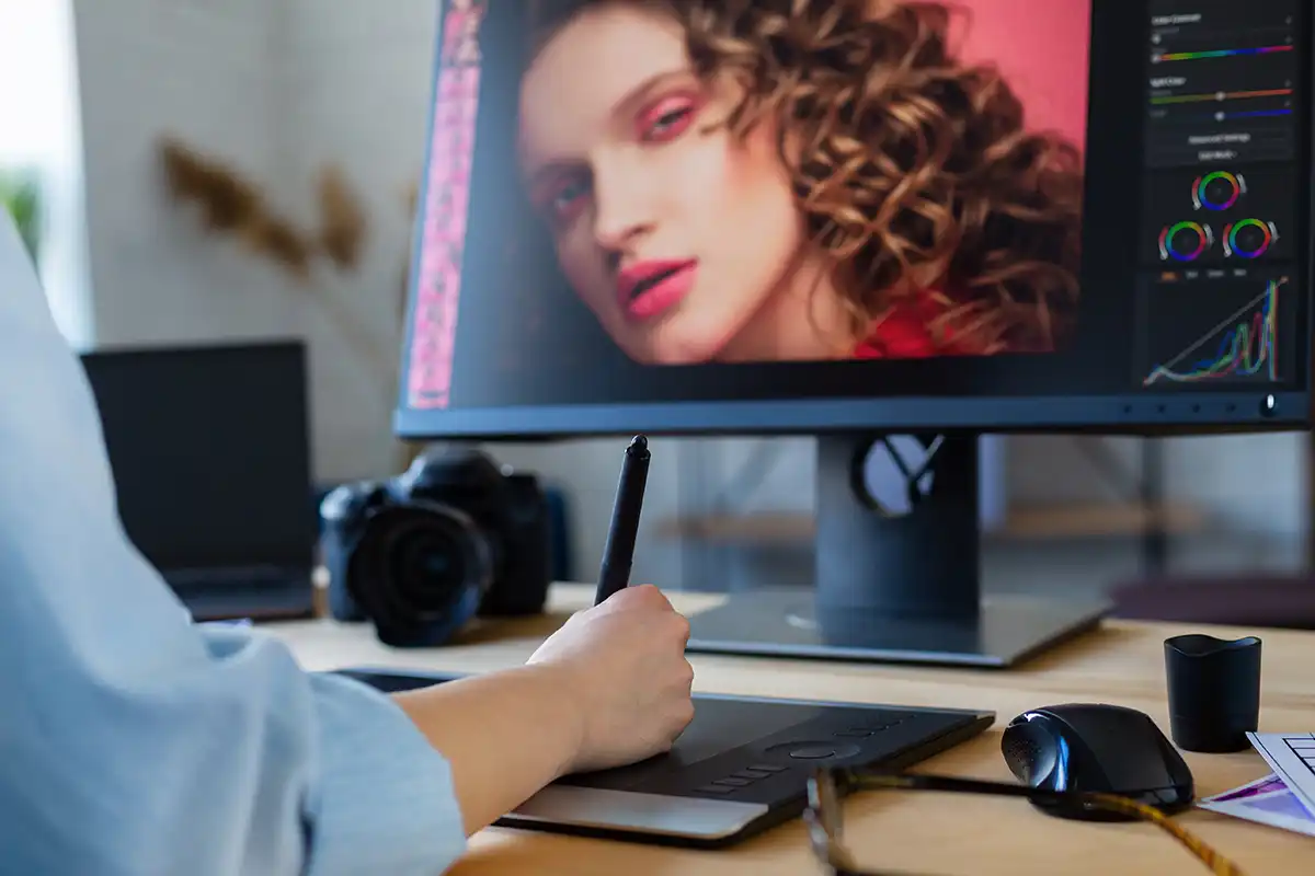 A digital retoucher sat at a desk retouching photos on a computer using a graphic stylus pen