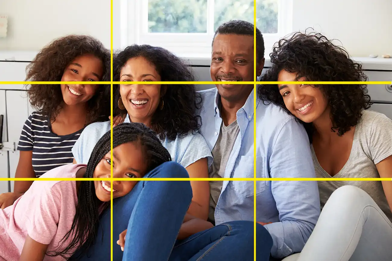 A family with three older daugthers and two parents cuddled up together on a sofa smiling at the camera