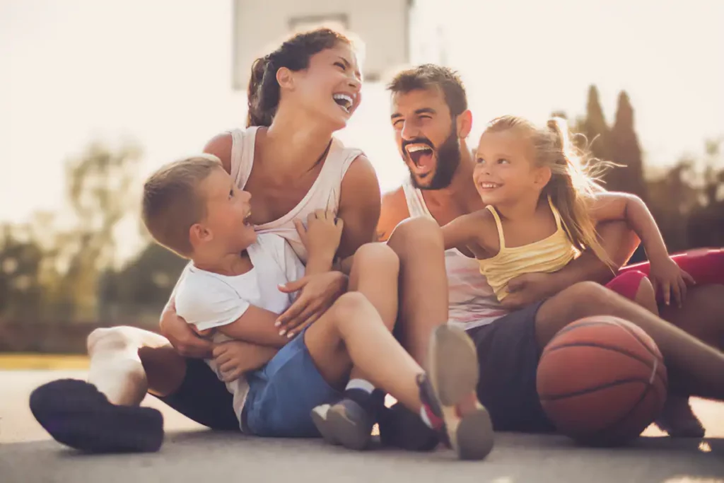 A family sat on a basketball court having a cuddle with the young children with a basketball in front of them