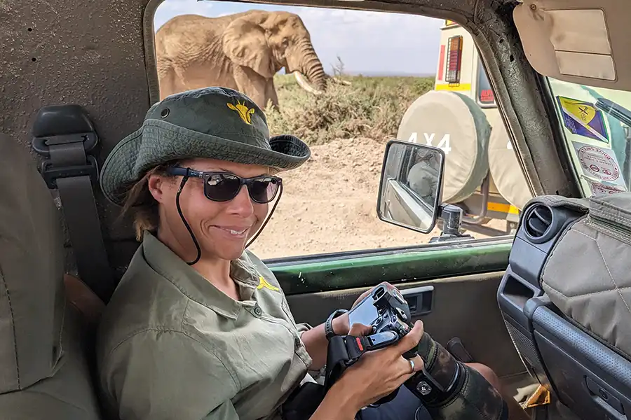 Wildlife photographer Rachel Sinclair holding a camera in a jeep with an elephant outside