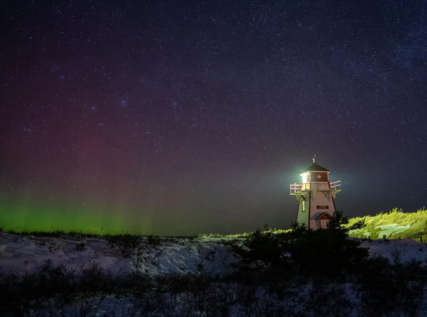 a lighthouse with a shining light on the night sky with northern lights