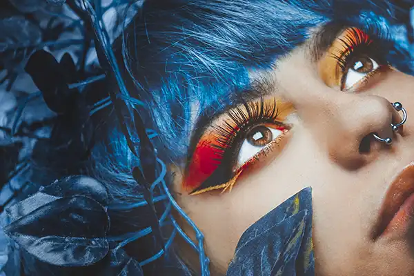 close up of a girl with blue hair and colour eye makeup lying down in blue flowers