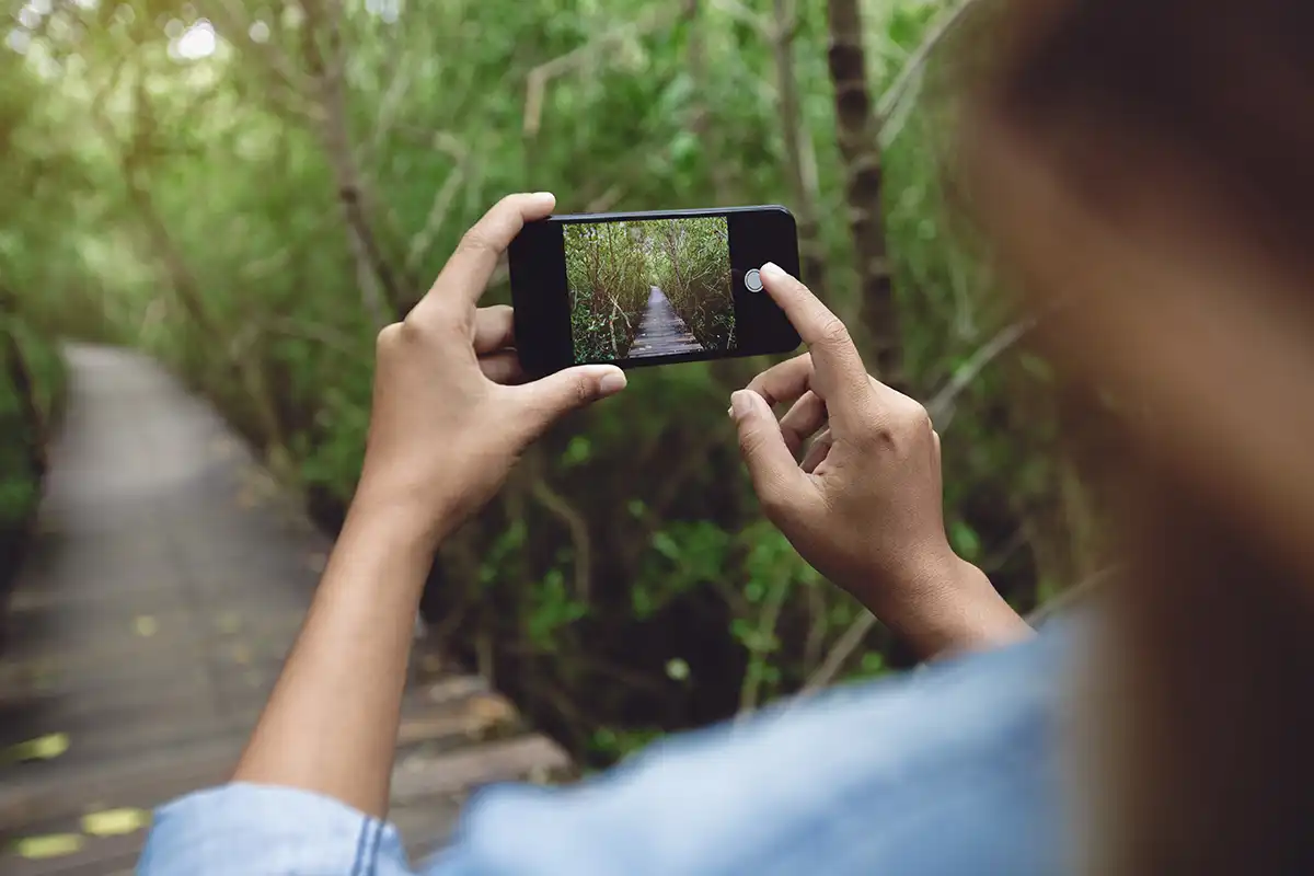 Woman holding an iPhone taking a photo down a path